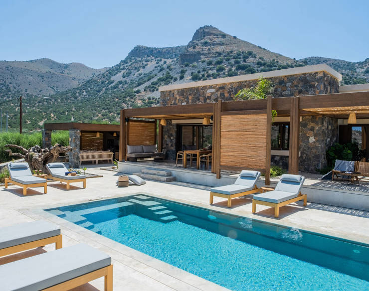 Luxury private pool area with sun loungers, shaded outdoor lounge and stone architecture at Elounda Naxia Villas