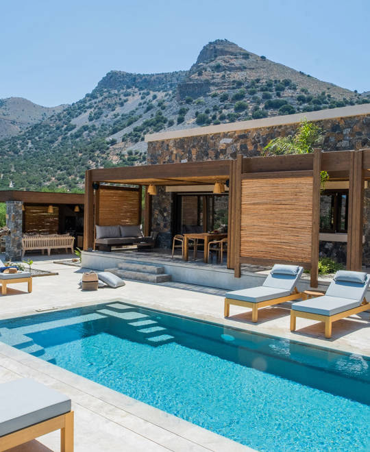 Luxury private pool area with sun loungers, shaded outdoor lounge and stone architecture at Elounda Naxia Villas