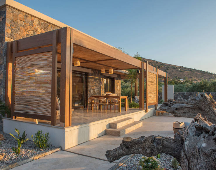 Stone-built villa terrace with wooden pergola, dining table, and shades, surrounded by olive treen in evening light