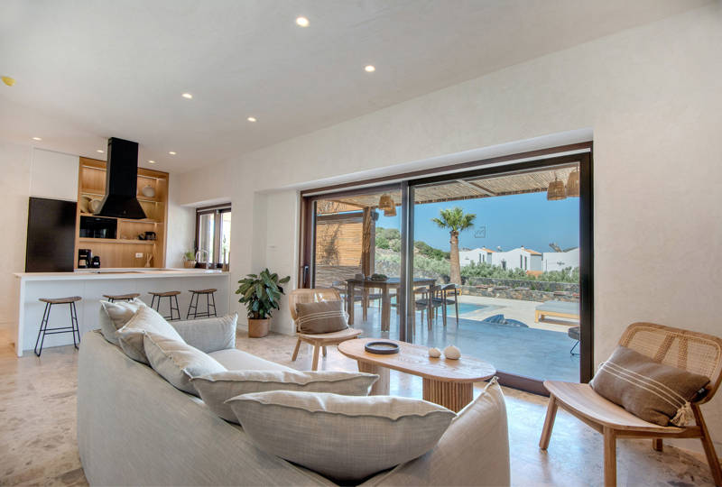 Bright living area at Elounda Naxia Villas with cozy furniture, and large glass doors accessing the terrace