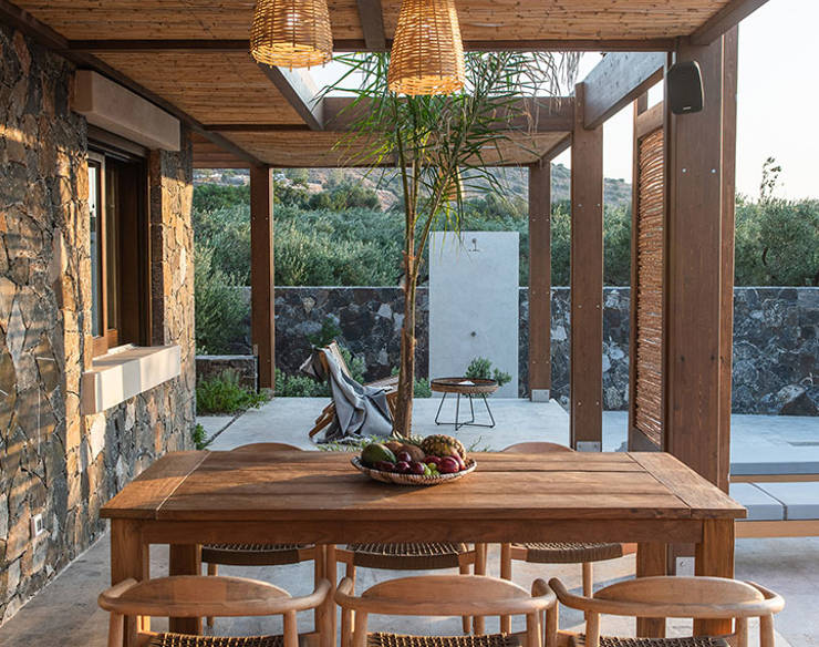 Outdoor dining area at Elounda Naxia Villas with a wooden table, woven chairs, and pendant lights under a pergola