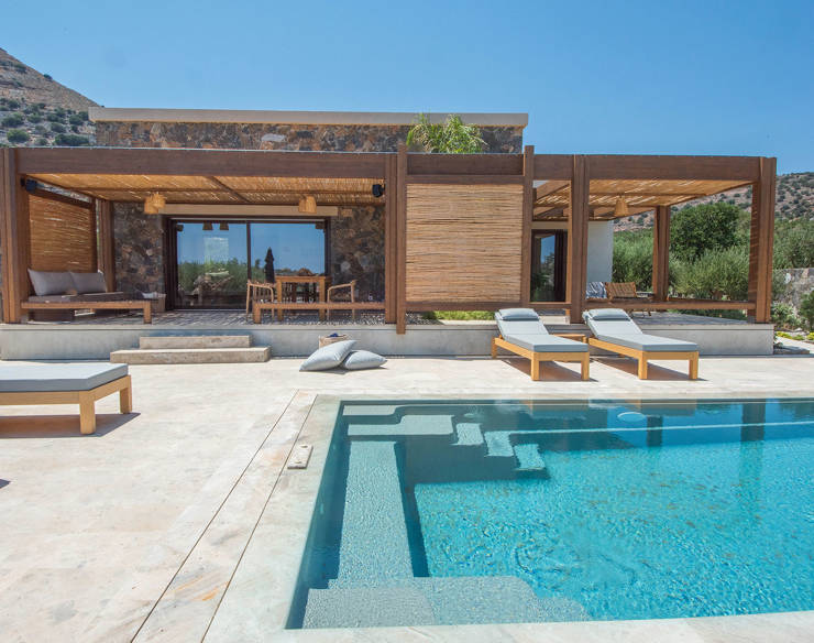 Private pool with sunbeds and shaded terrace area at Elounda Naxia Villas, with stone walls and mountain view