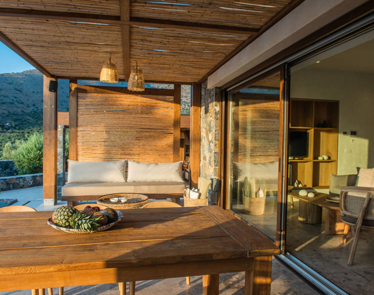 Covered outdoor seating area at Elounda Naxia Villas with wooden table, sofa, and panoramic view