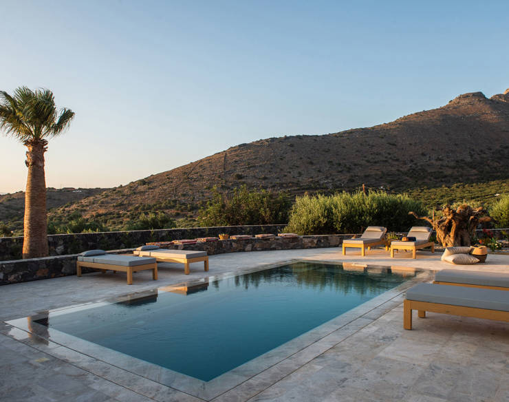 Tranquil pool area at Elounda Naxia Villas during sunset, with wooden loungers, palm tree and mountain view