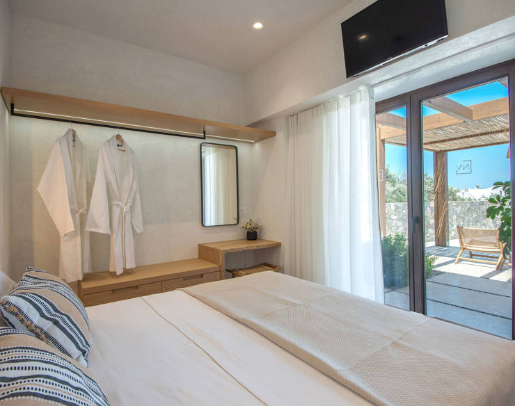 Master bedroom at Elounda Naxia Villas with soft lighting, modern decor, an patio access through glass doors