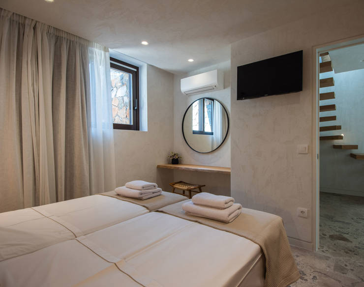 Modern guest bedroom at Elounda Naxia Villas with twin beds, round mirror, and view of wooden staircase