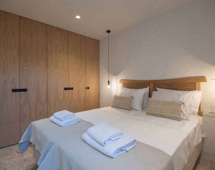 Warm twin bedroom at Elounda Naxia Villas with wooden wardrobe, woven headboard, and soft pendant lighting