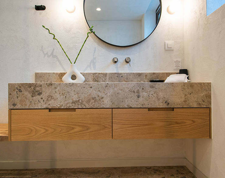 Modern bathroom vanity at Elounda Naxia Villas with round mirror, stone countertop, wooden drawers, and soft lighting