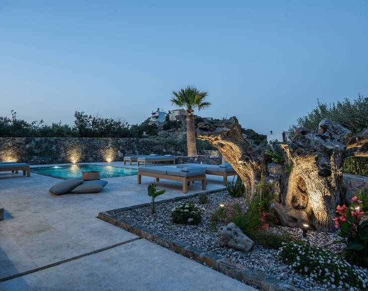 Evening view of Elounda Naxia Villas pool area with soft lighting, loungers and illuminated olive tree