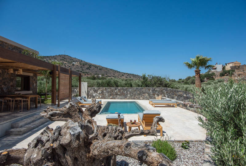 private pool at Elounda Naxia Villas surrounded by sun loungers, stone walls and Mediterranean garden