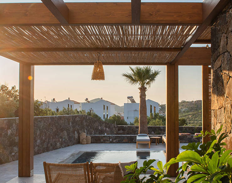 Private patio at Elounda Naxia Villas with wooden pergola, pool view, and lounge chairs at sunset