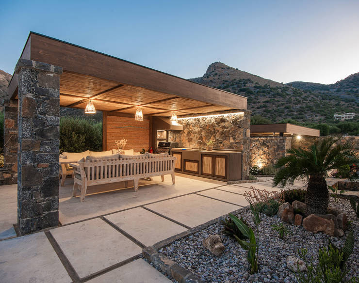 Evening view of the outdoor dining and BBQ area at Elounda Naxia Villas, with stone walls and wooden ceiling