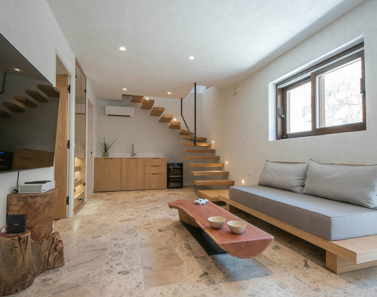 Living area at Elounda Naxia Villas featuring floating wooden stairs, minimalist sofa, stone floor and wall-mounted TV
