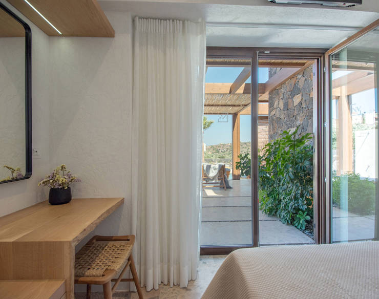 Elegant master bedroom at Elounda Naxia Villas with wooden desk and terrace access through glass doors